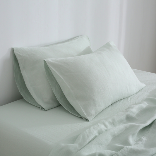 A set of sage hemp pillowcases on a bed, with the pillows partially visible.