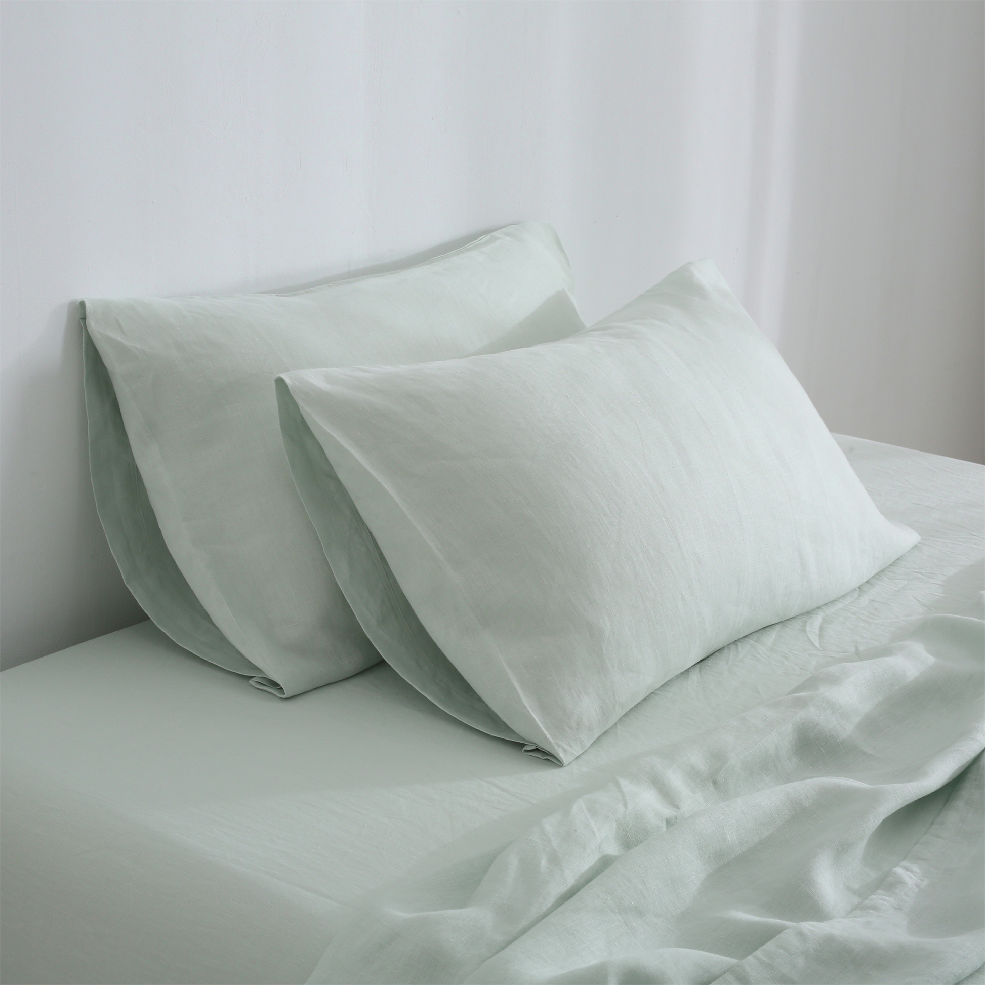 A set of sage hemp pillowcases on a bed, with the pillows partially visible.