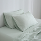 A set of sage hemp pillowcases on a bed, with the pillows partially visible.